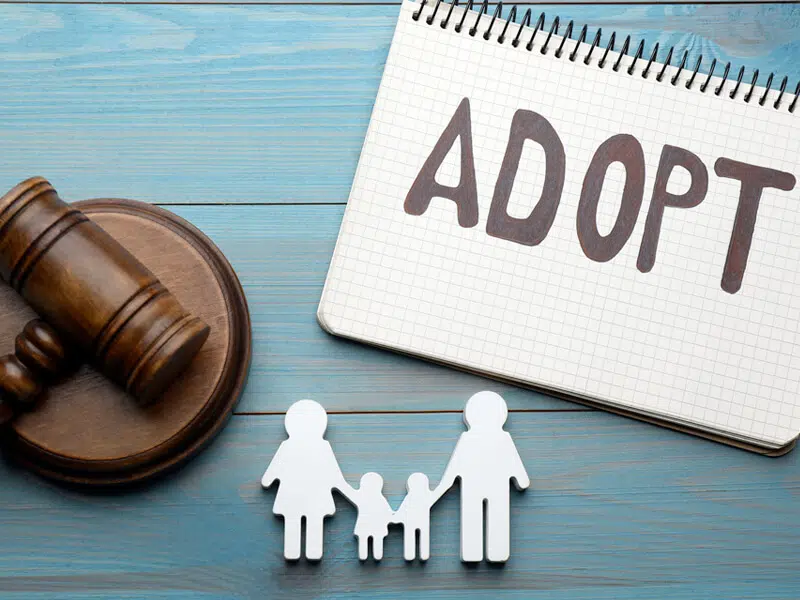 Our Tarrant County Adoption lawyer helps families with the adoption process. This picture has a gavel indicating the court, a legal pad that has "Adopt" written on it and a family paper cutout.